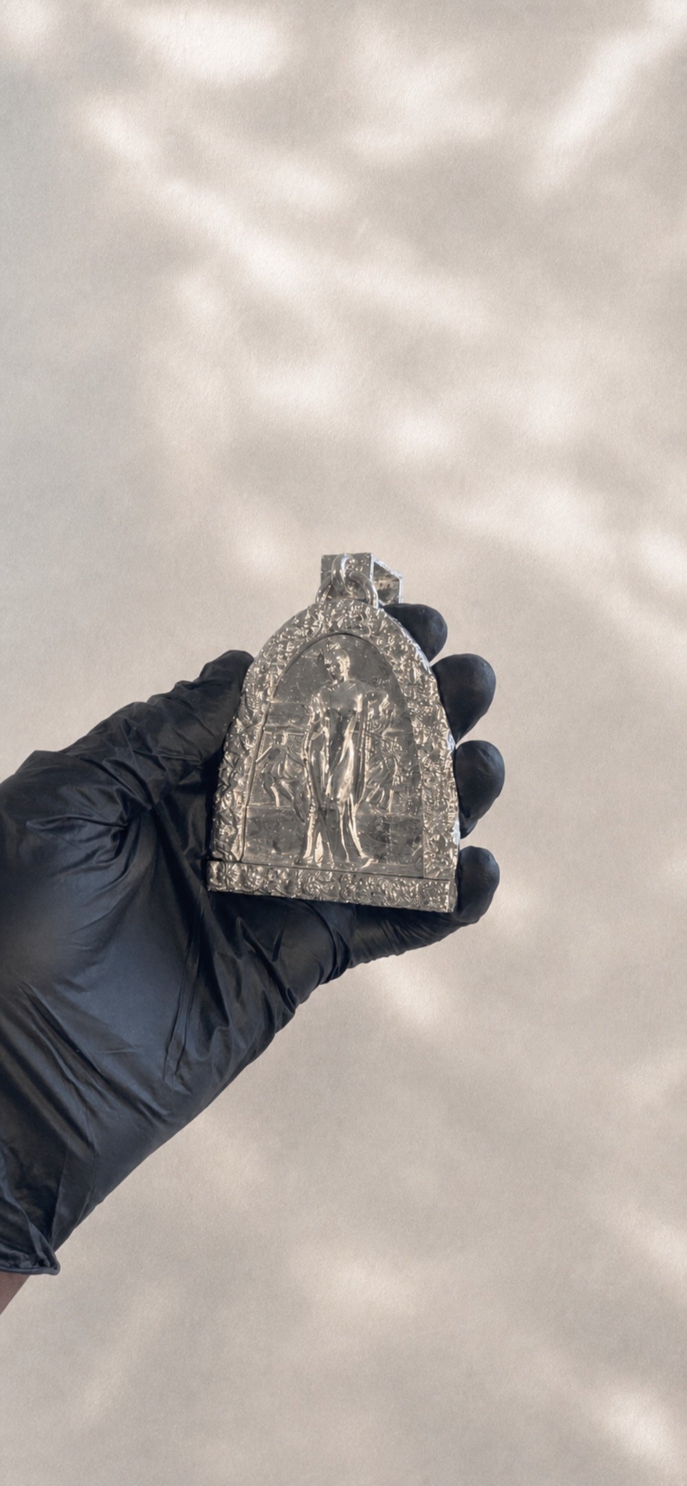 Reverse of a sculptural silver PRJCT RLGN pendant held in a gloved hand